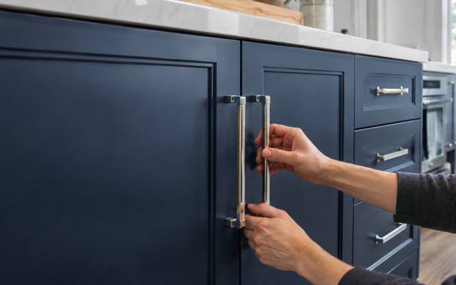 A hand fitting a chrome handle to a navy painted cabinet door.